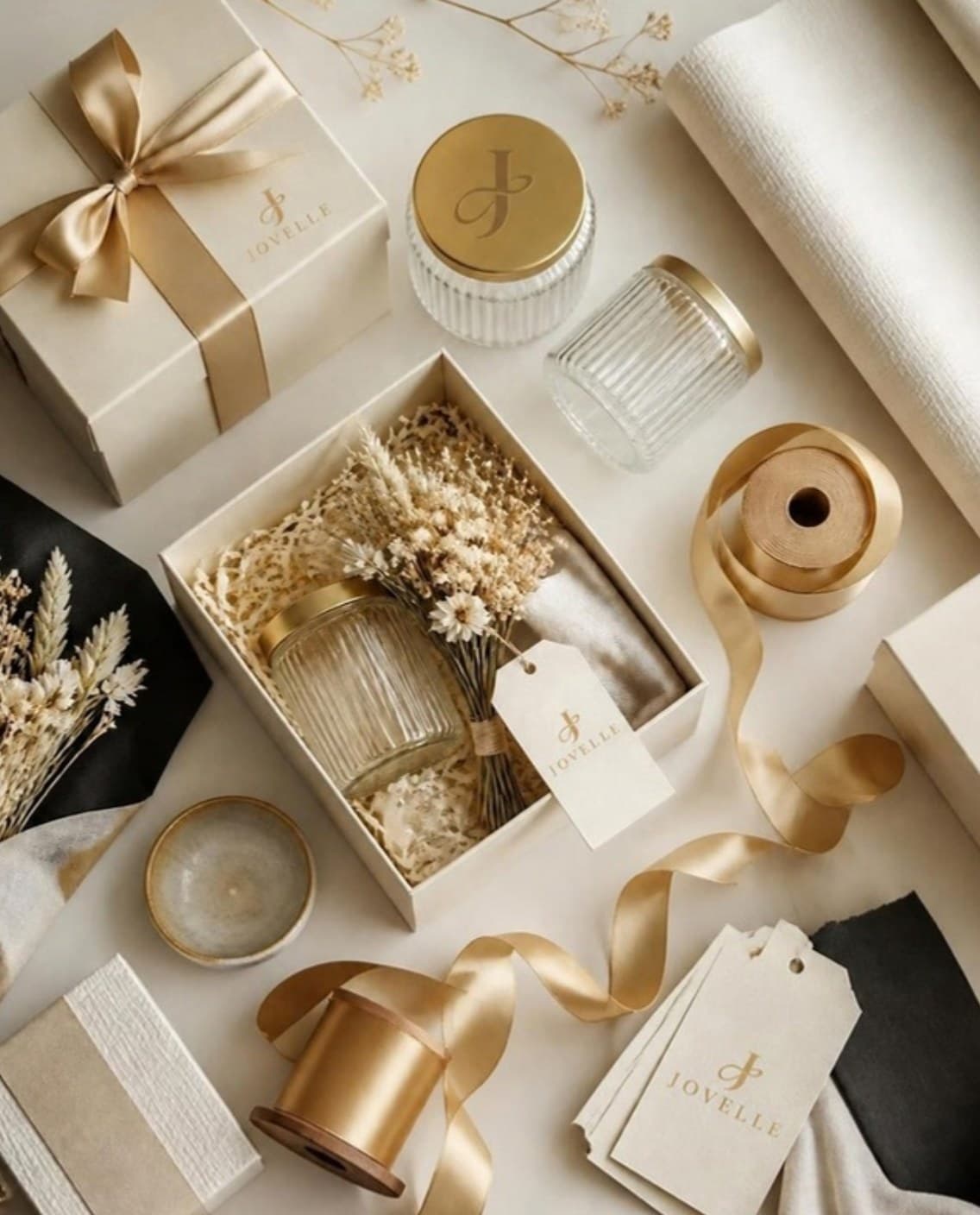 Glass jars, cream boxes, gold satin ribbon and ivory wrapping paper laid out on a cream surface